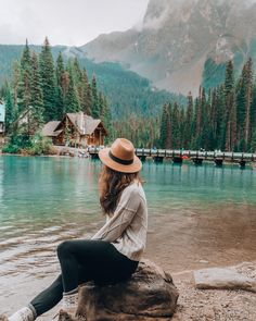 a woman sitting on top of a rock next to a lake