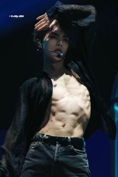 a shirtless male performing on stage with his hair blowing in the wind and wearing jeans