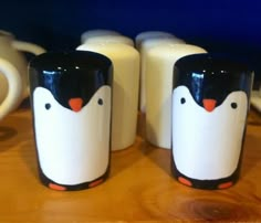 three penguin mugs sitting next to each other on a wooden table with milk in front of them