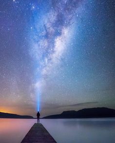 a person standing on a pier looking up at the stars in the sky above them