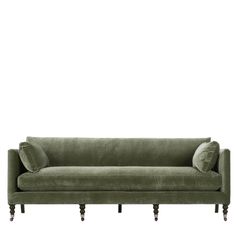 a green velvet couch with two pillows on it's back and one arm extended