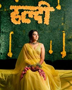 a woman in a yellow sari sitting on a stage with flowers around her neck