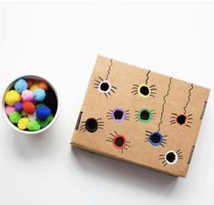 a box filled with different colored balls next to a bowl of pom - poms