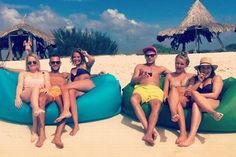 four people sitting on bean bag chairs at the beach with straw huts in the background