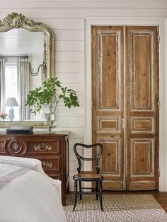 an antique chair sits in front of a large wooden door and mirror on the wall