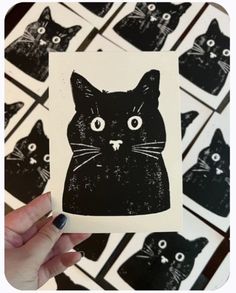 a person holding up a black cat sticker in front of many smaller black cats