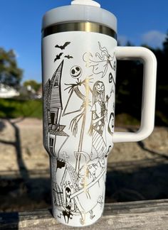 a white travel mug with halloween images on it sitting on a wooden table in front of a blue sky