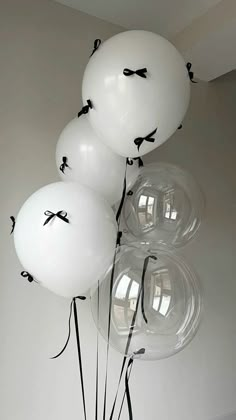 white balloons with black bows tied to them are in a vase on the floor next to a wall