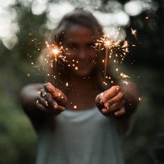 a woman holding sparklers in her hands with trees in the backgrouf