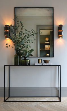 a mirror and some plants on a shelf in a room with white walls, wood floors and flooring