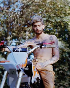 a man with tattoos standing next to a motorcycle