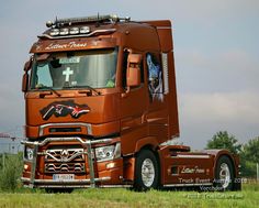 an orange semi truck parked on top of a lush green field