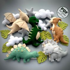 several felt dinosaurs are shown together on a gray background with white clouds and green leaves