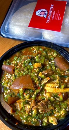 a black bowl filled with food on top of a wooden table next to a container of rice