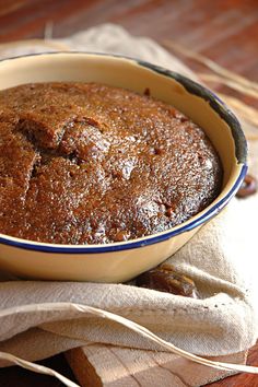 a brown cake in a blue and white dish on a cloth next to some cinnamon sticks