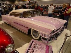 an old pink car is on display in a showroom with people looking at it