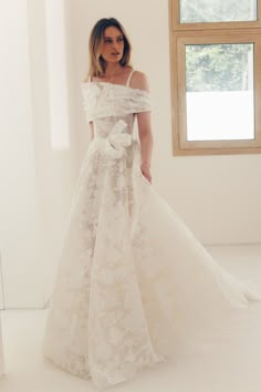 a woman in a white wedding dress is standing by a window and looking at the camera