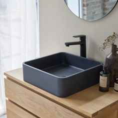 a bathroom sink sitting on top of a wooden counter next to a mirror and bottle