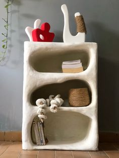 a white shelf with some books and vases on it's sides next to a wall