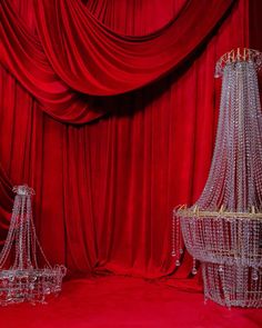 three crystal chandeliers are on display in front of red curtained walls and drapes