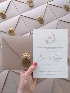 a person holding up a wedding card and envelope with some coins on the table next to it