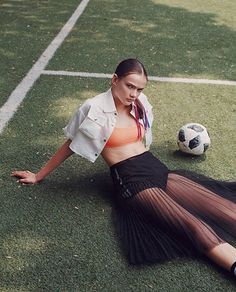 a woman laying on the ground next to a soccer ball wearing an orange top and black skirt