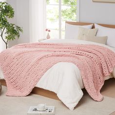 a bed with a pink blanket on top of it next to a potted plant