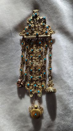 This very ornate chatelaine is fire gilded on brass. It is studded throughout with small Persian turquoise and is ornately hand chased and pierced. The chatelaine is 5 inches long (without the added drops), by 2 inches wide. It has later added fobs and a perfume with out the lid. The piece at some point was repaired with soft solder (please see pic) and the clip removed and a pin added. This has no doubt been loved over its life. It is a wonderful piece of history. C. 1830 and possibly French. F Persian Jewelry, Soft Solder, Persian Turquoise, Antique Clothing, Ancient Jewelry, Chatelaine, Favorite Jewelry, Brooch Pin, Brooches