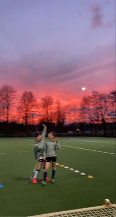 two girls are playing soccer at sunset on the field with their arms in the air