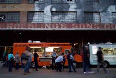 people standing in line at an orange food truck on the side of a building with graffiti painted on it