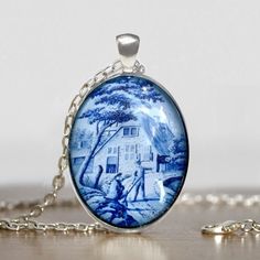 a blue and white porcelain pendant with a house in the background on a silver chain