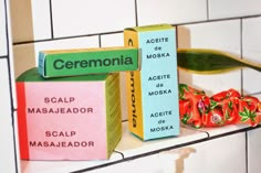 a shelf with two boxes and some fake flowers on top of it, in front of a tiled wall