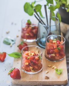 three glasses filled with fruit and nuts on top of a wooden cutting board next to a potted plant