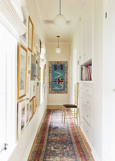 a long hallway with white walls and pictures on the wall, along with a colorful rug