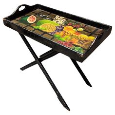 a tray with fruit and vegetables painted on the top is sitting on a metal stand