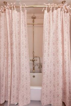 a bath tub sitting next to a window covered in pink curtains with flowers on them