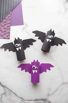 some paper bats are sitting on a marble table with purple and black decorations in the background