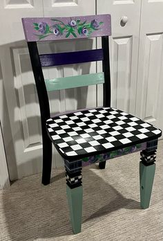 a black and white checkered chair sitting in front of a door with flowers painted on it