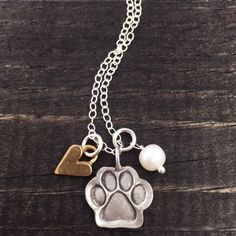 a dog's paw and heart charm on a wooden table with a pearl necklace