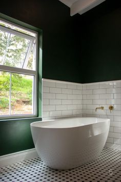 a large white bath tub sitting next to a window in a green walled bathroom