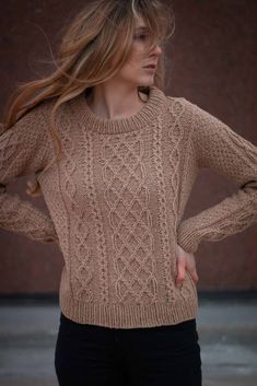 a woman wearing a brown sweater and black pants with her hair blowing in the wind