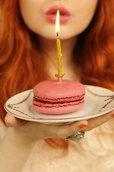 a woman holding a plate with a pink cake on it and a lit candle in the middle