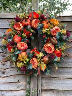 a wreath with orange flowers and greenery hanging on a wooden fence next to a tree