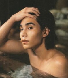 a young man sitting in a hot tub with his hand on his head