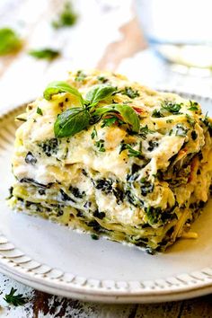 a white plate topped with lasagna covered in cheese and spinach garnish