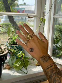 a person's hand with tattoos on it near a window and potted plants