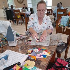 a woman sitting at a table working on a laptop computer surrounded by quilts and fabrics