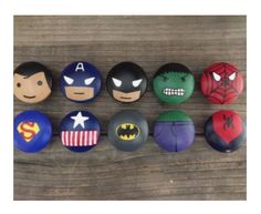 a bunch of different types of buttons on a wooden surface with the faces of superheros painted on them