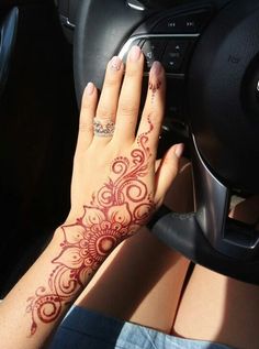 a woman's hand on the steering wheel of a car with henna tattoos