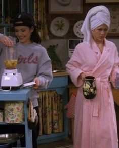 two women standing in a kitchen with one holding a blender and the other wearing a towel